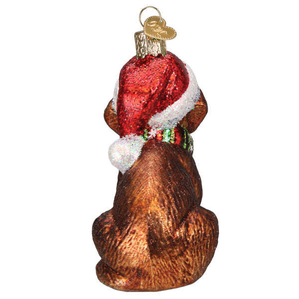 Back view of a glass chocolate Labrador pup ornament wearing a red Santa hat and green scarf.