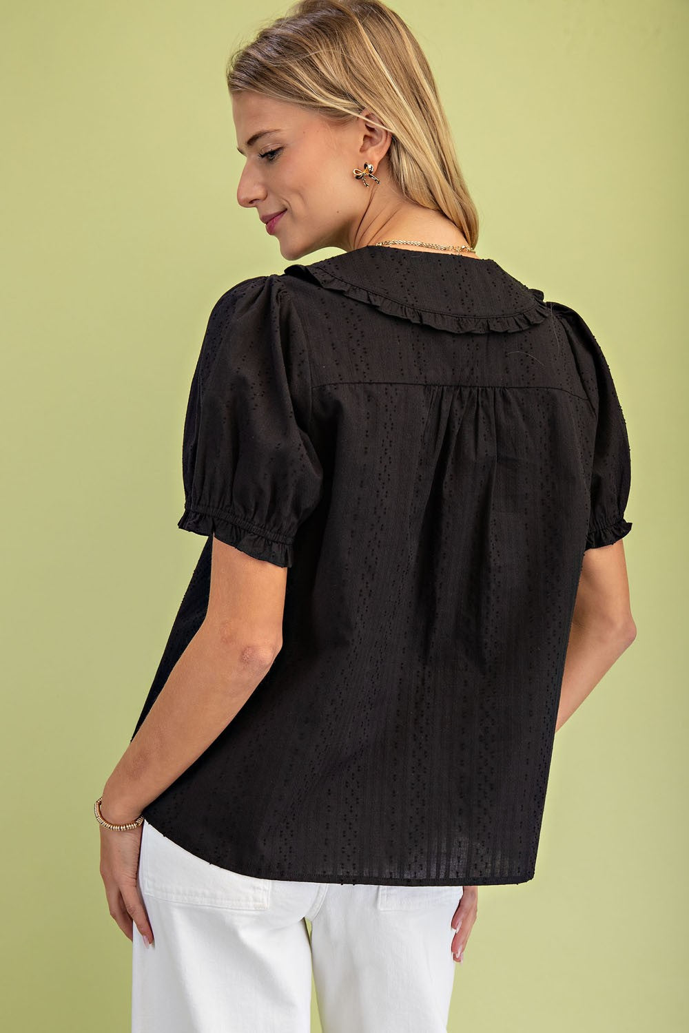 Back view of a woman wearing a black short puff sleeve blouse with a ruffled Peter Pan collar.
