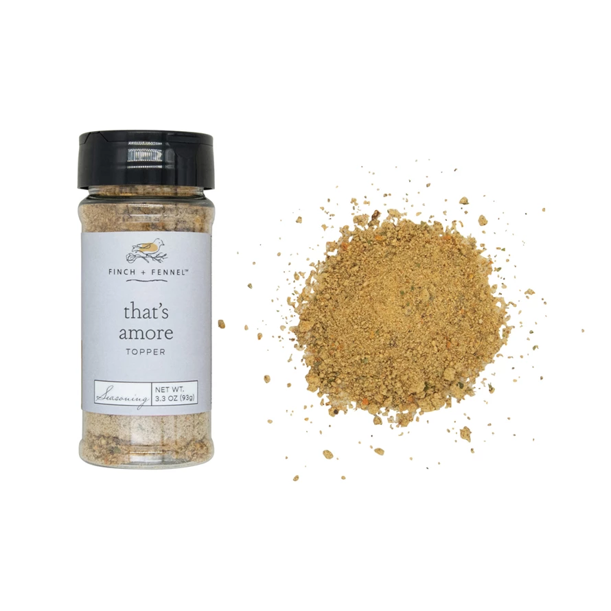 Finch + Fennel That's Amore Topper Seasoning in a 3.3 oz jar next to a pile of the spice blend.