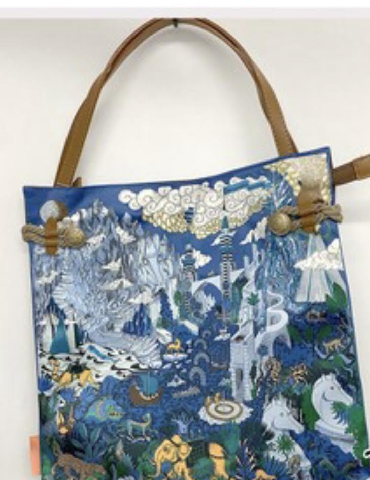 Boho scarf tote bag with blue silk-like body, intricate landscape pattern, and brown shoulder straps.