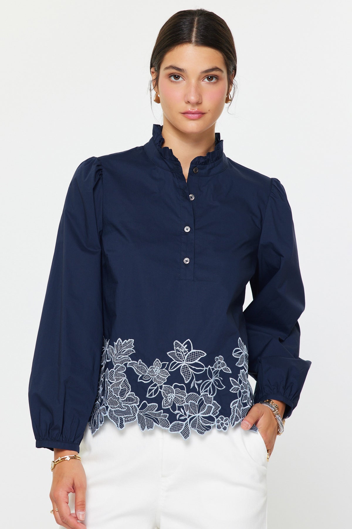 Lucy embroidered long sleeve blouse in cotton poplin with ruffle stand collar, button front closure, and floral embroidery at hem.