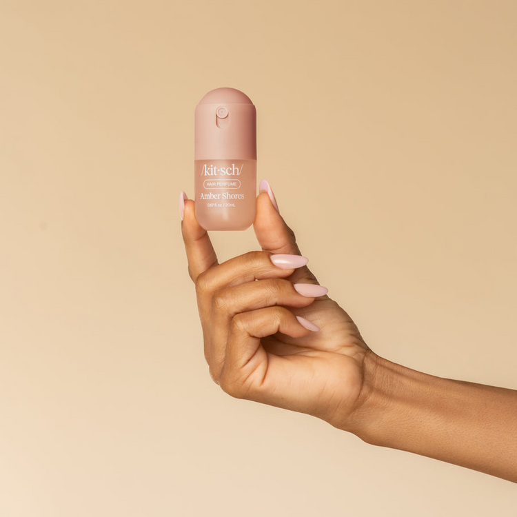 A hand holding a mini pink bottle of Kitsch Amber Shores Hair & Body Perfume Mist.
