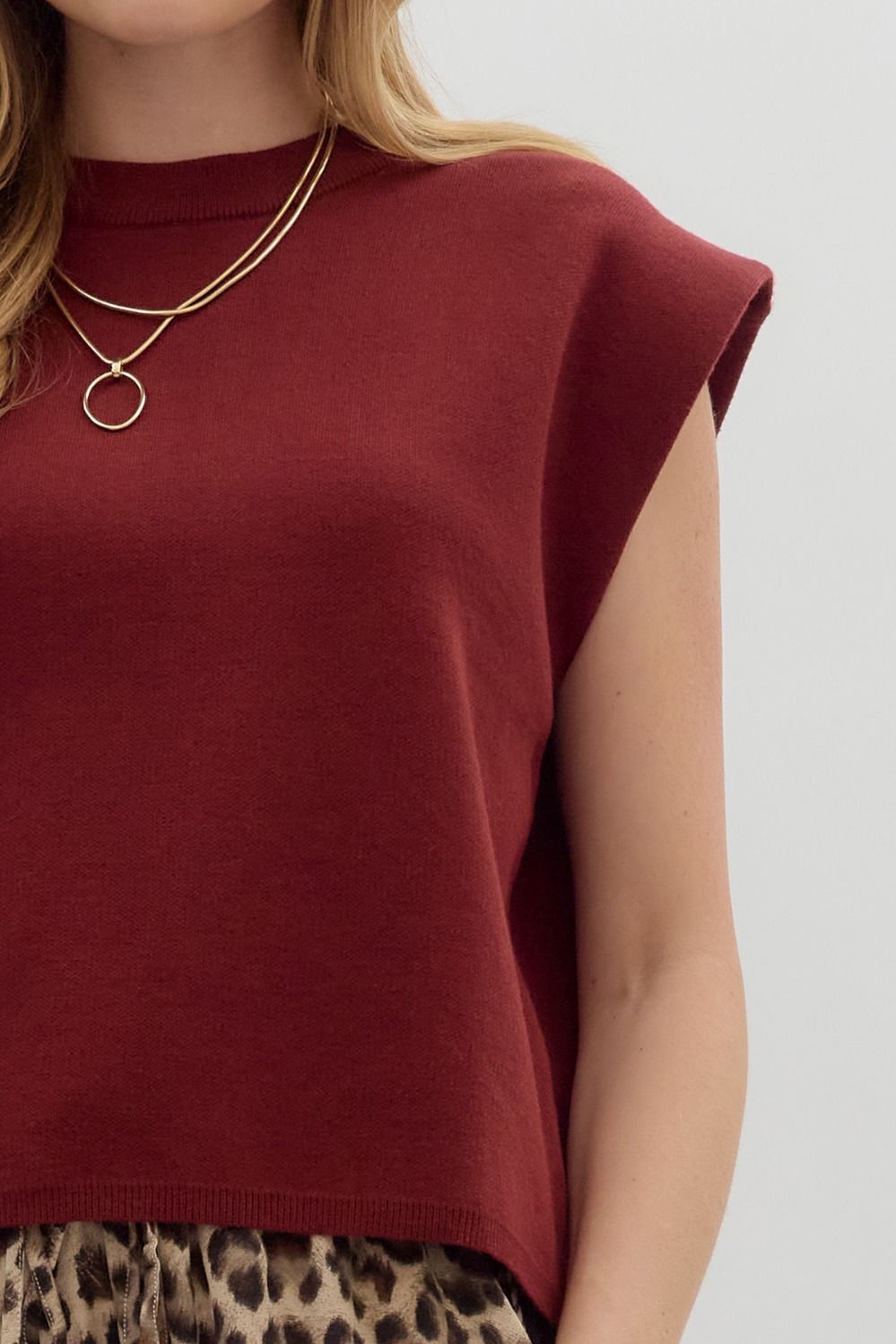 Close-up of a burgundy crewneck knit muscle tee top with a gold necklace and leopard print pants.