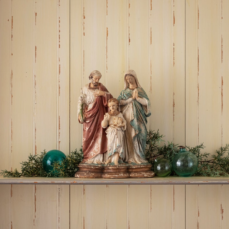 A 16-inch resin Holy Family statue with an aged, antique finish on a shelf with green ornaments.