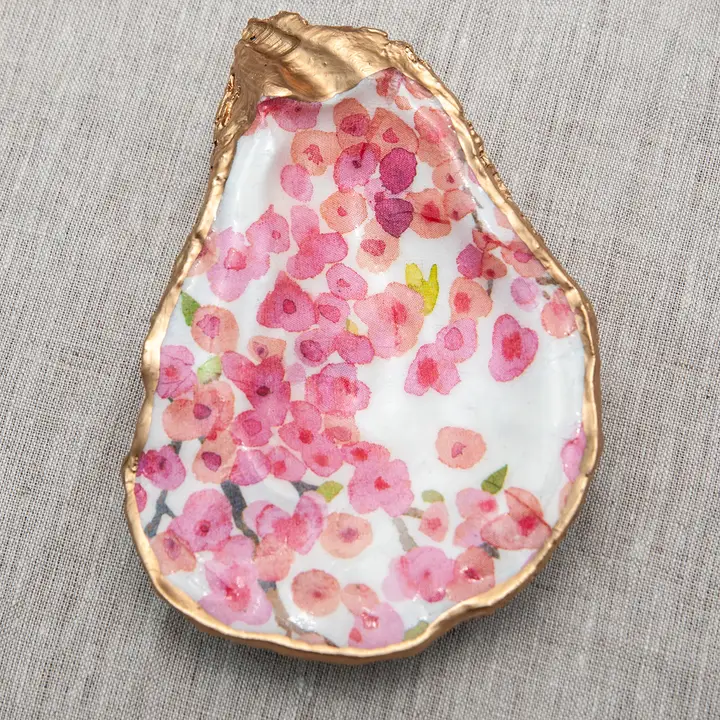 Decoupaged oyster shell with pink floral pattern and metallic gold trim on a linen background.