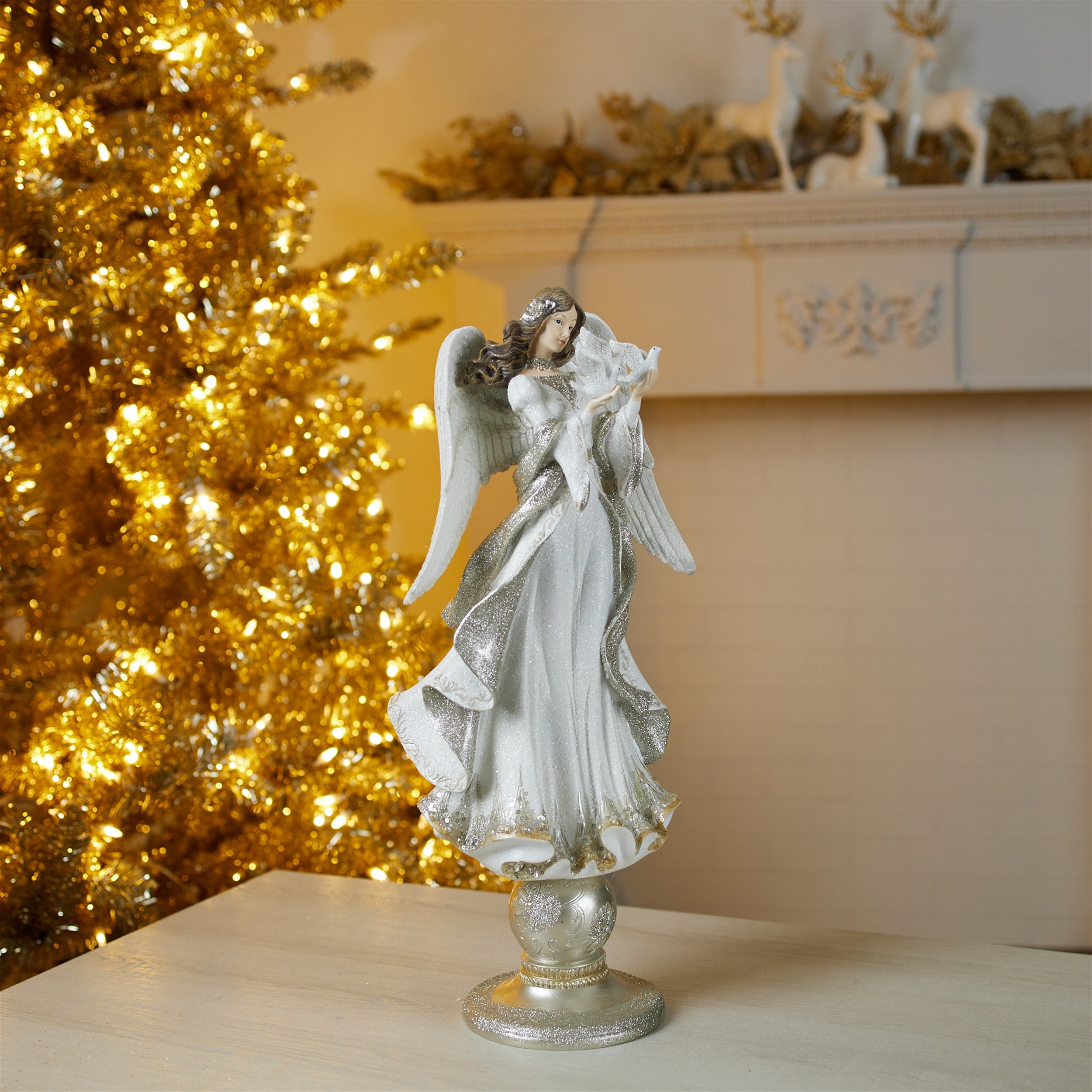 A 20-inch tall resin angel figurine holding a dove, standing on a pedestal by a gold Christmas tree.