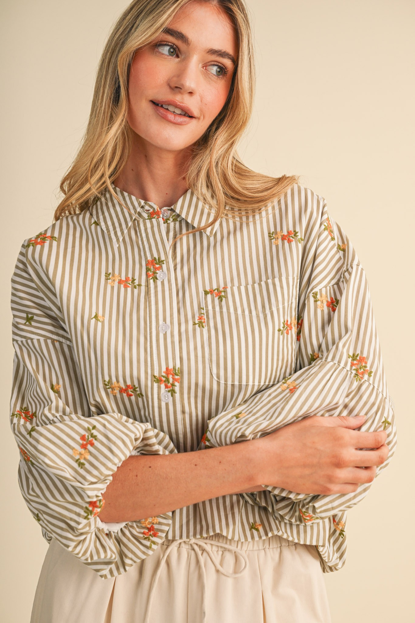 Woman wearing a striped button-down top with floral embroidery and bubble sleeves.