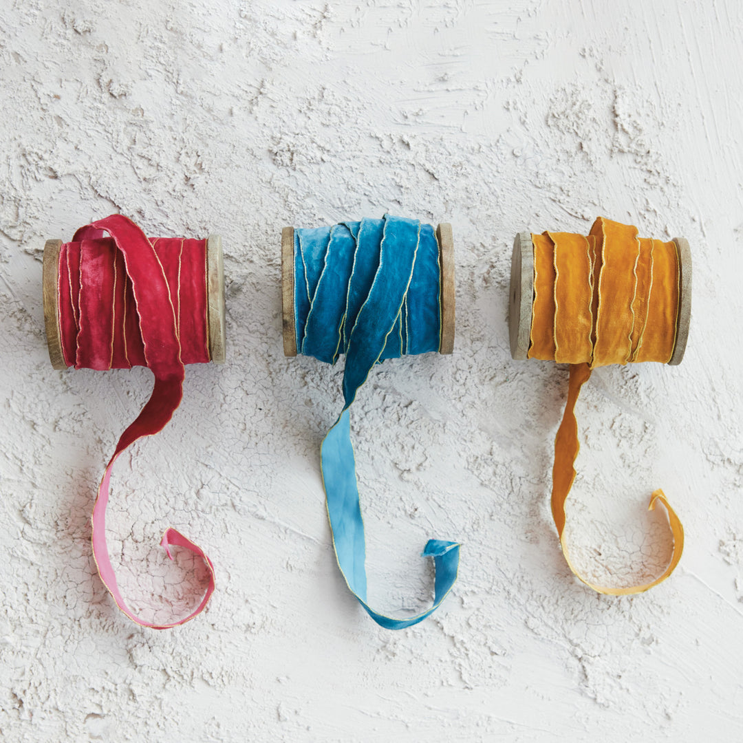 Three spools of 3/4 inch velvet ribbon in red, blue, and gold with metallic edges on wood spools.