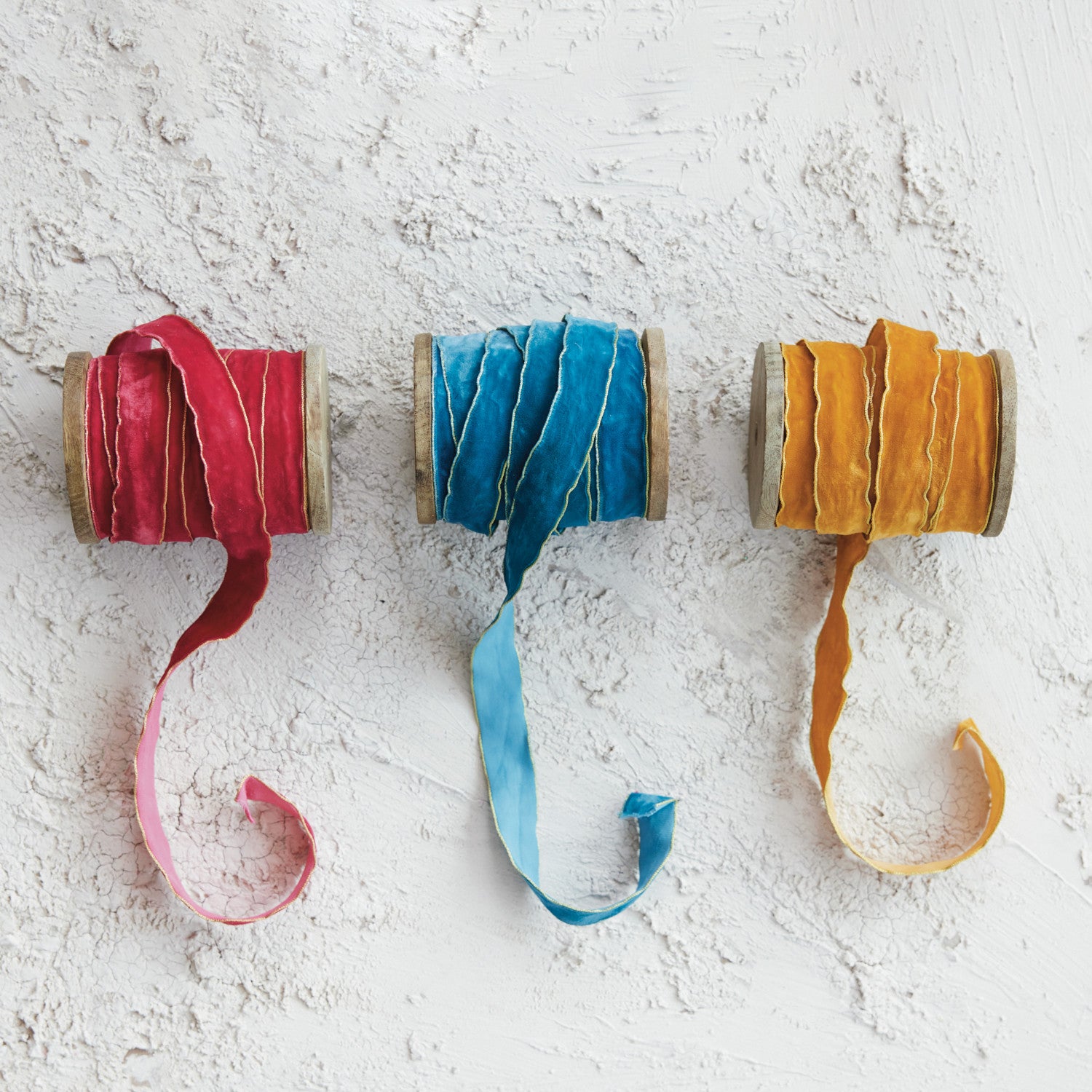 Three spools of 3/4 inch velvet ribbon in red, blue, and gold with metallic edges on wood spools.