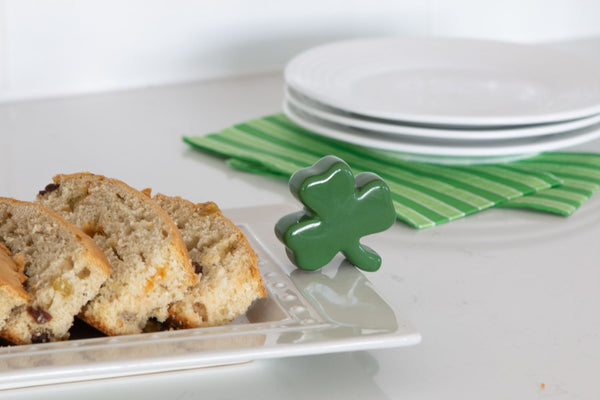 Green ceramic shamrock decoration on a white platter with sliced Irish soda bread.