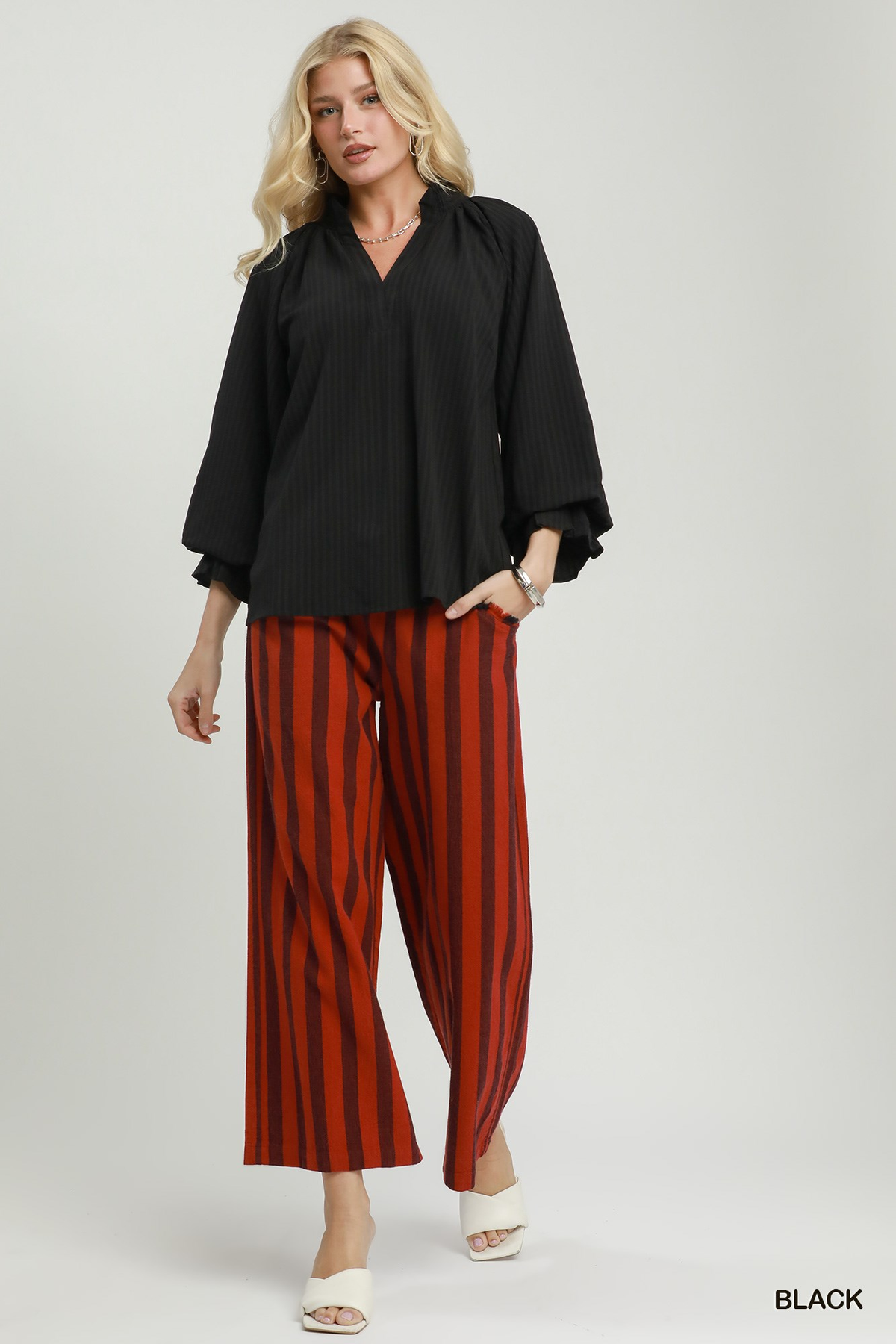 Woman wearing the Emma Stripe Split Neck Blouse in black with red striped wide-leg trousers.