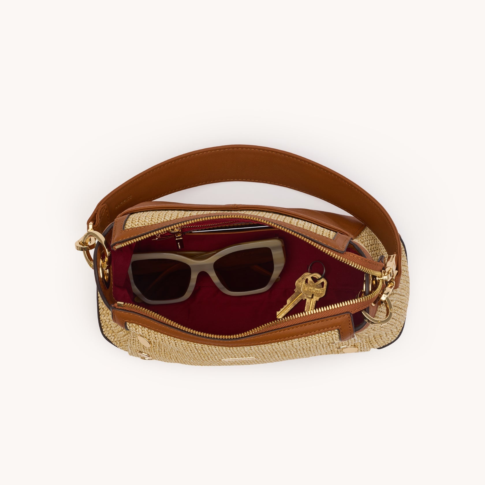 Top view of the Bryant Med Cocoa Raffia bag open, showing red lining, sunglasses, and keys inside.