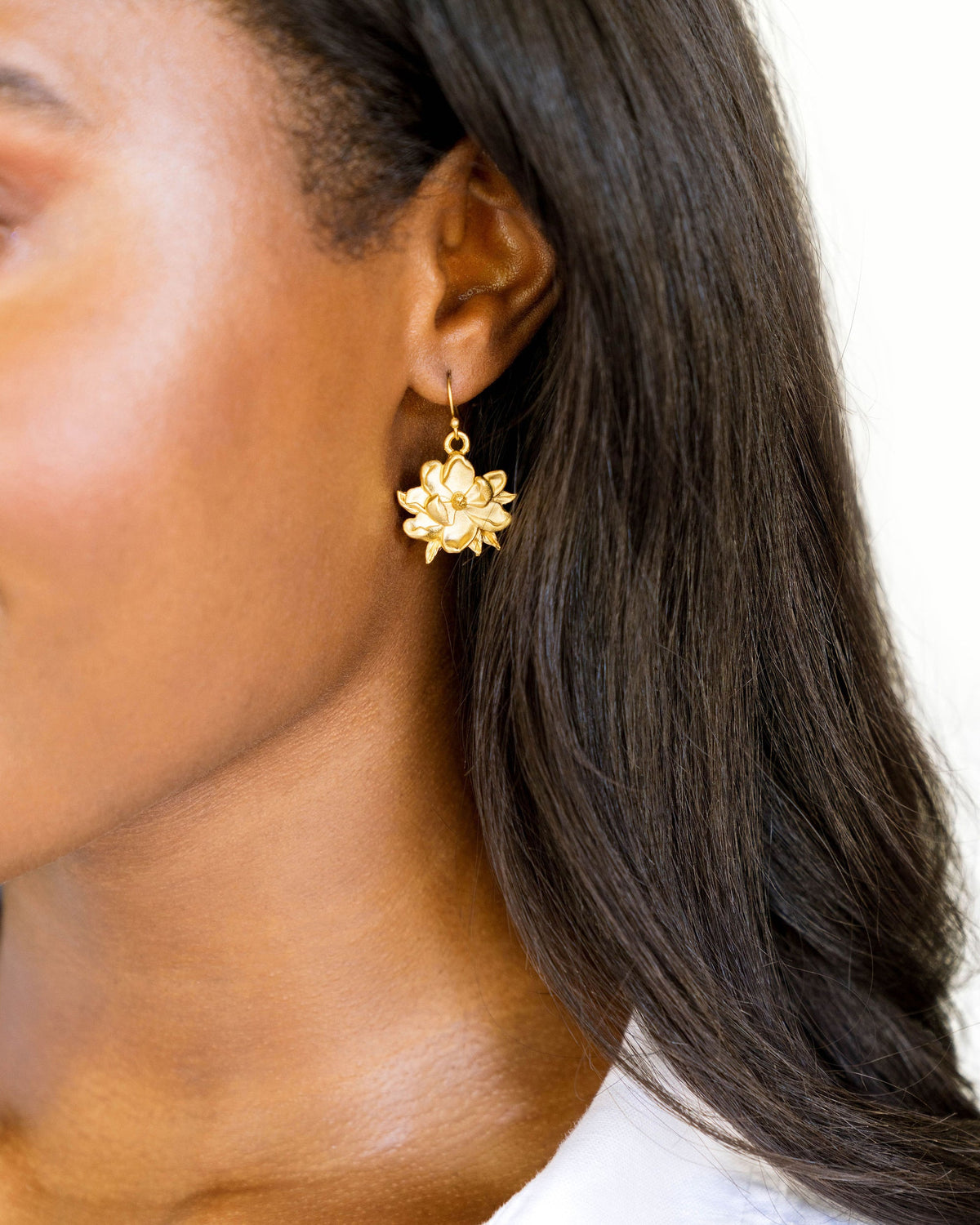 Gold-tone floral earrings shaped like magnolias, dangling from a woman's ear.
