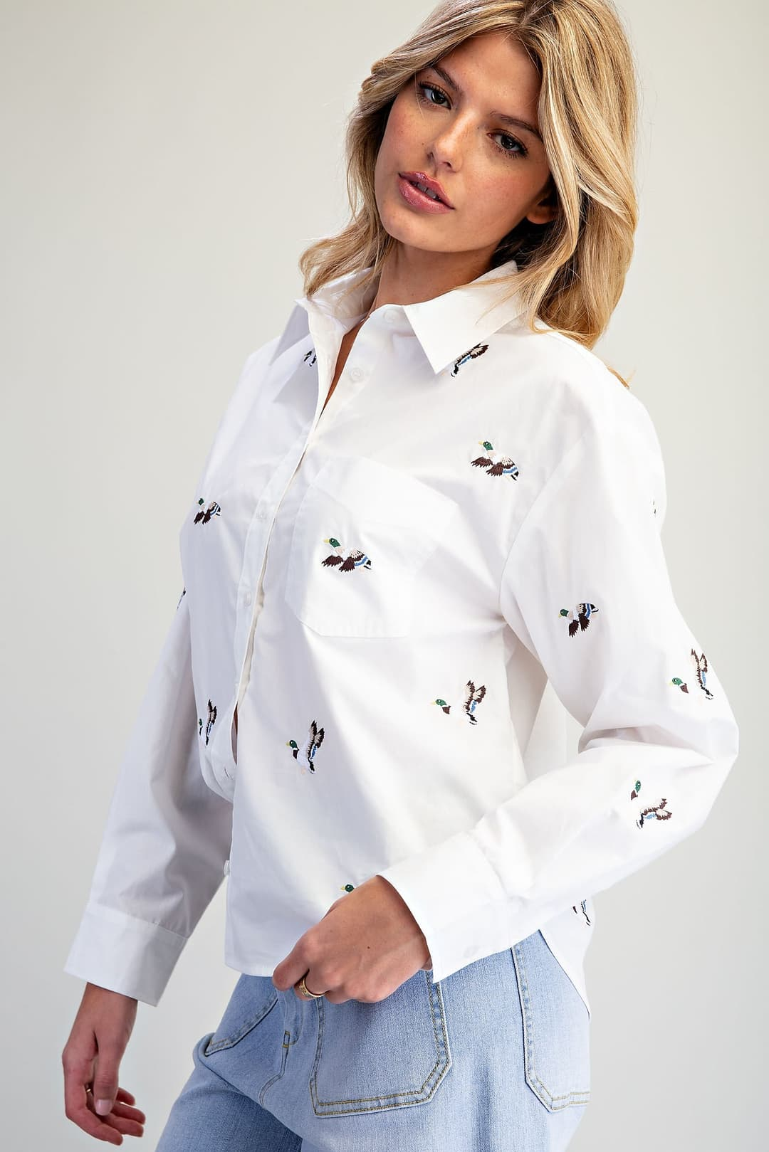 Woman wearing the Lainey white button down shirt with embroidered mallard duck motifs.