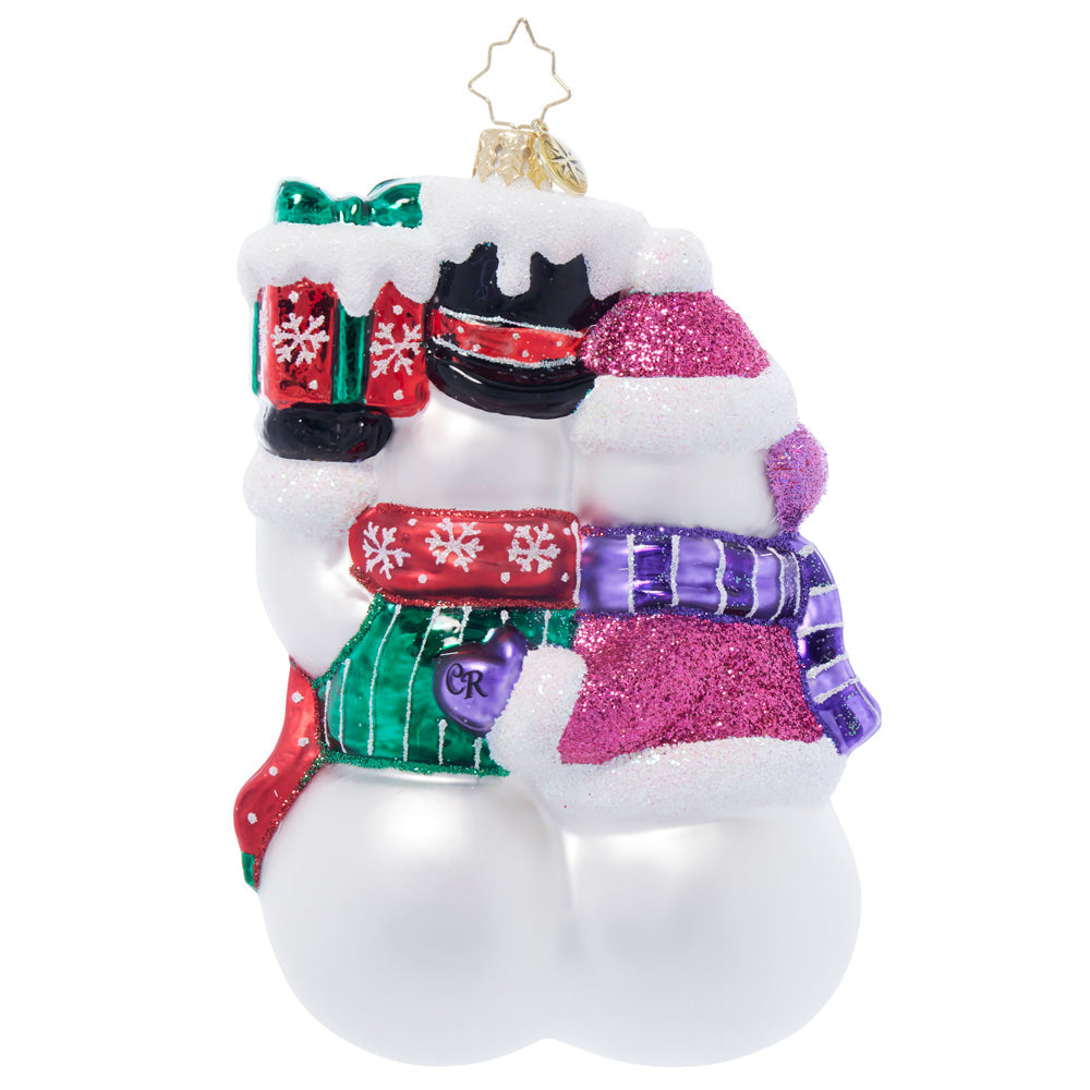 Glass Christmas ornament of a snow couple hugging, featuring glittery hats, scarves, and gifts.