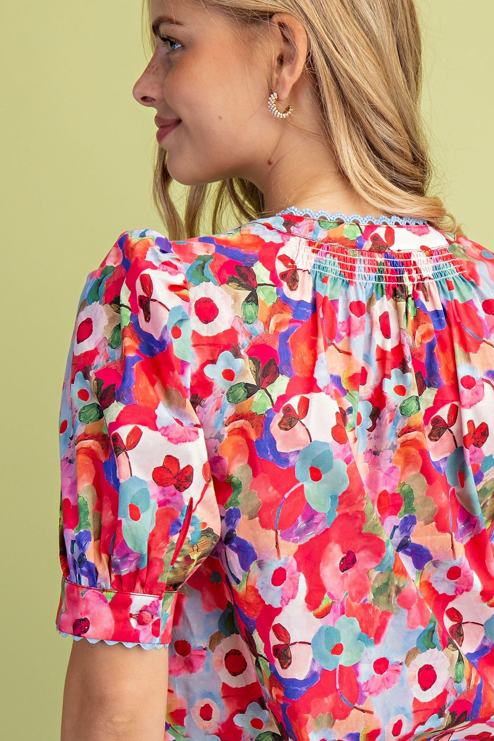 Back view of a woman wearing a red floral blouse with smocking and blue ric-rac trim.