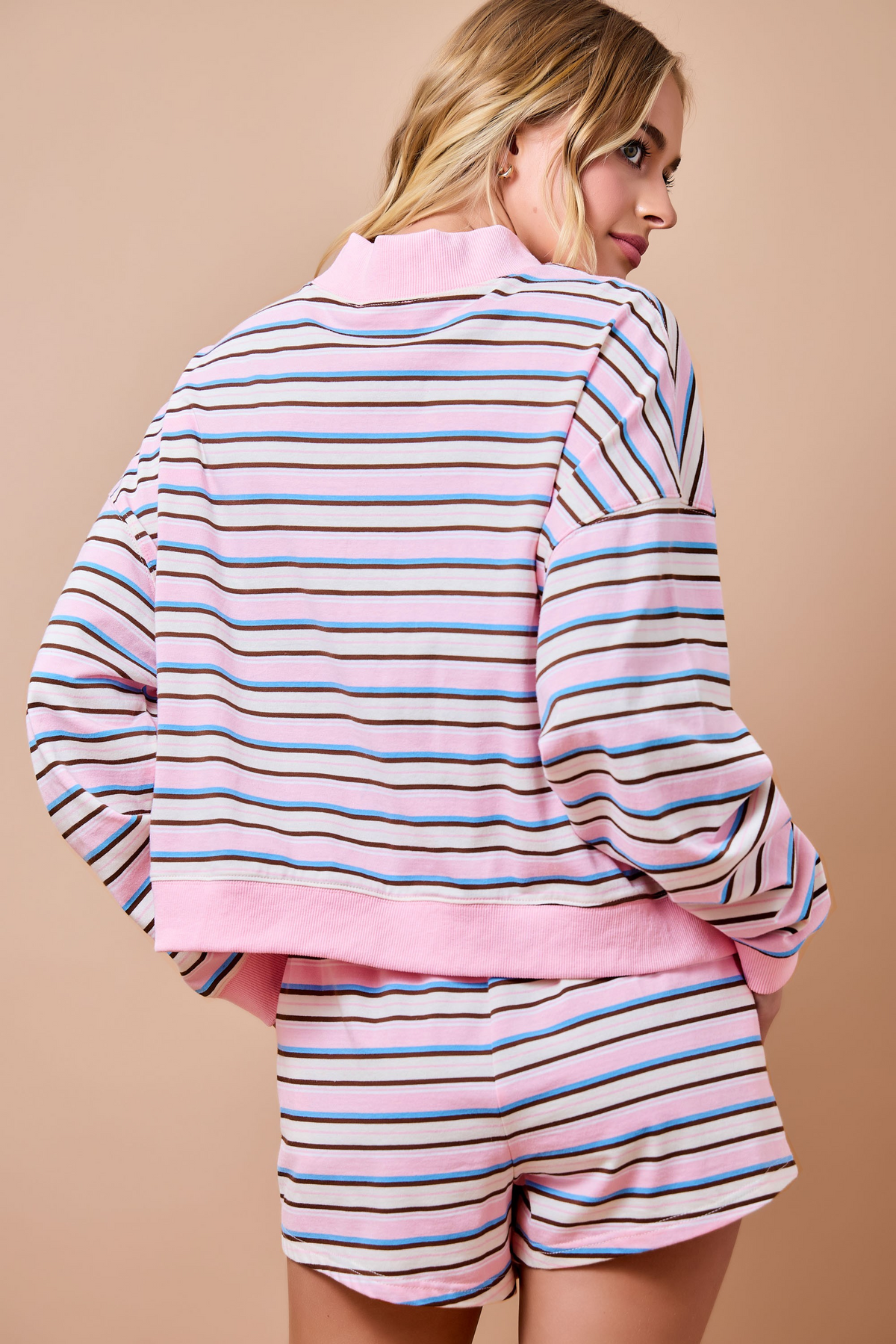 Back view of a woman wearing a pink, blue, and brown striped loose fit lounge sweatshirt and shorts.