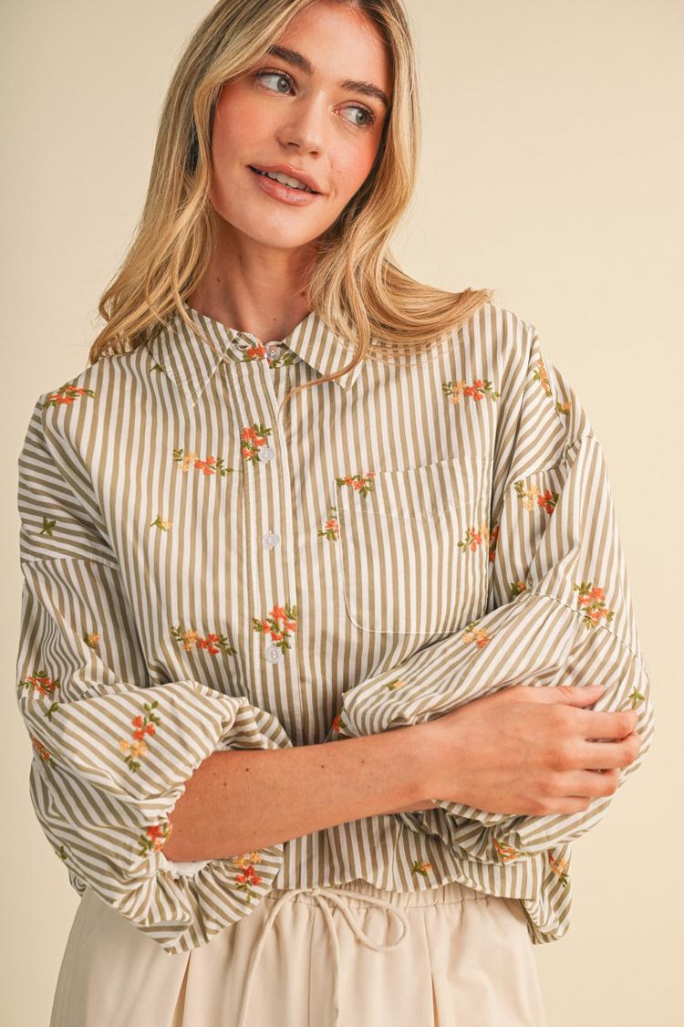 Woman wearing a striped floral embroidery button-down top with bubble sleeves and a collared neck.