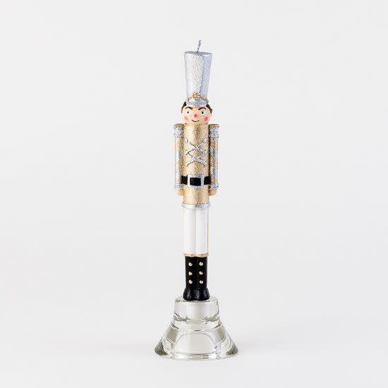 10 inch nutcracker taper candle in gold, white, and silver standing in a glass holder.