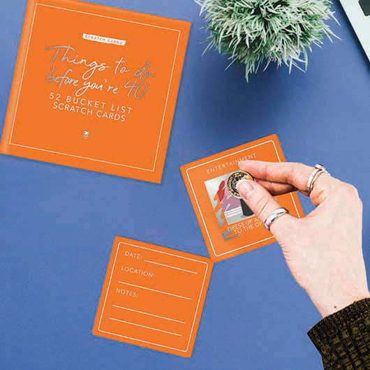 Orange 'Things to do before you're 40' bucket list scratch cards with a hand scratching one off.