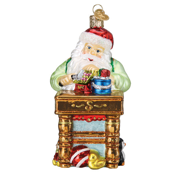 Glass Workshop Santa ornament featuring Santa at a workbench with toys and a penguin.