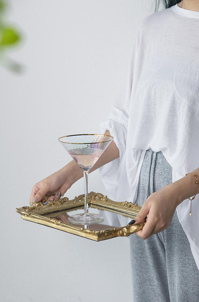 Gold ornate mirror tray with handles holding a martini glass with pink liquid.