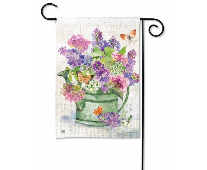 Green watering can overflowing with pink and purple lilacs and hydrangeas, with three orange butterflies.