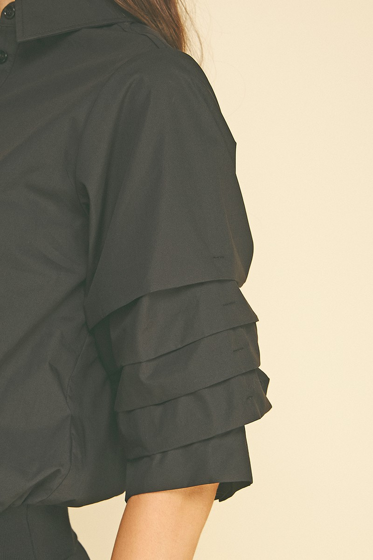 Close-up of the pleated sleeve detail on a black Jaycee cropped shirt with a classic collar.