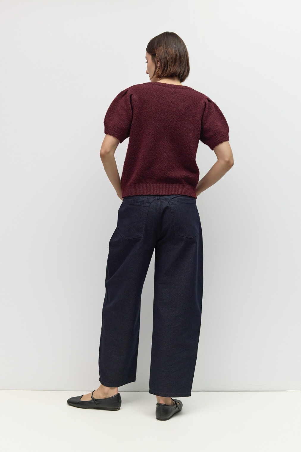 Back view of a person wearing a burgundy short puff sleeve knit top and dark wide-leg jeans.