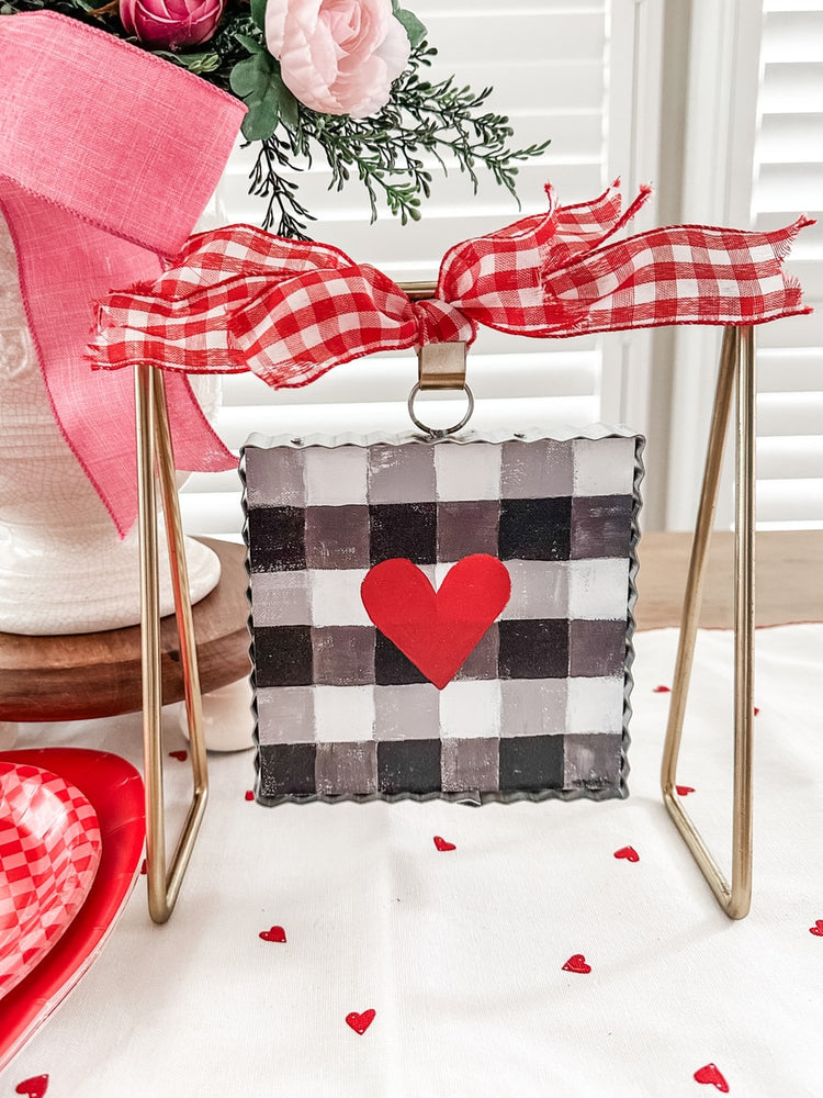 Gold metal gallery art stand displaying a buffalo plaid heart sign with a red gingham bow.