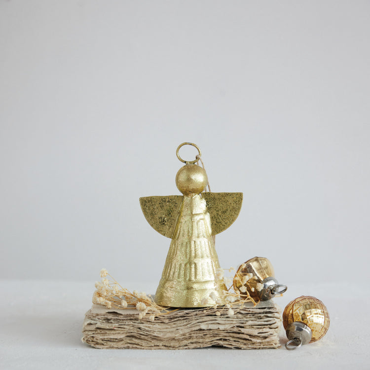 Gold finish metal angel ornament standing on a stack of paper with small gold baubles.
