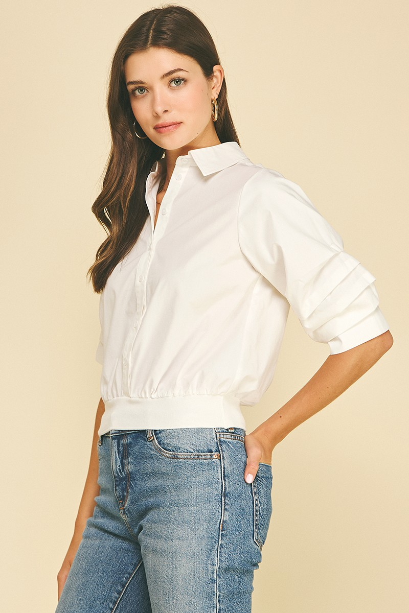 Woman wearing a white Jaycee cropped button-down shirt with pleated sleeves and a banded hem.