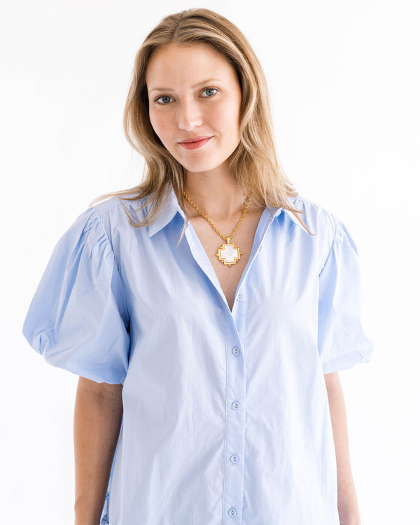 Woman wearing a gold chain necklace with a white mother of pearl cross pendant.