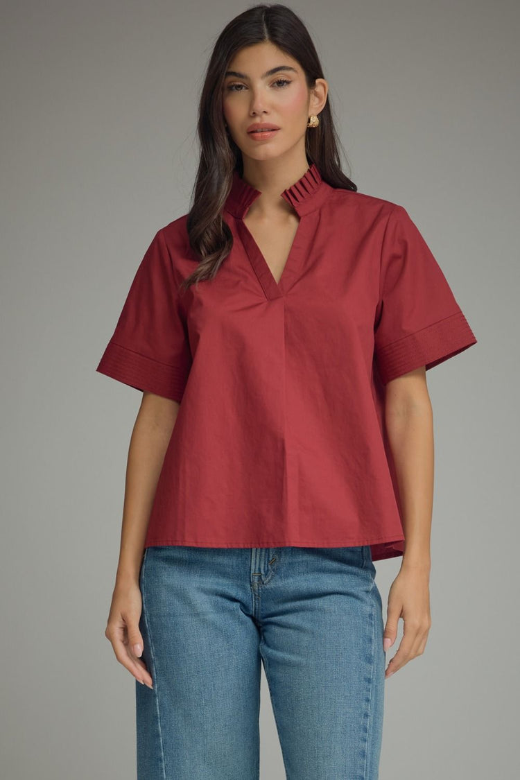 Woman wearing a red Addison short sleeve flare top with a pleated neck band and V-neckline.