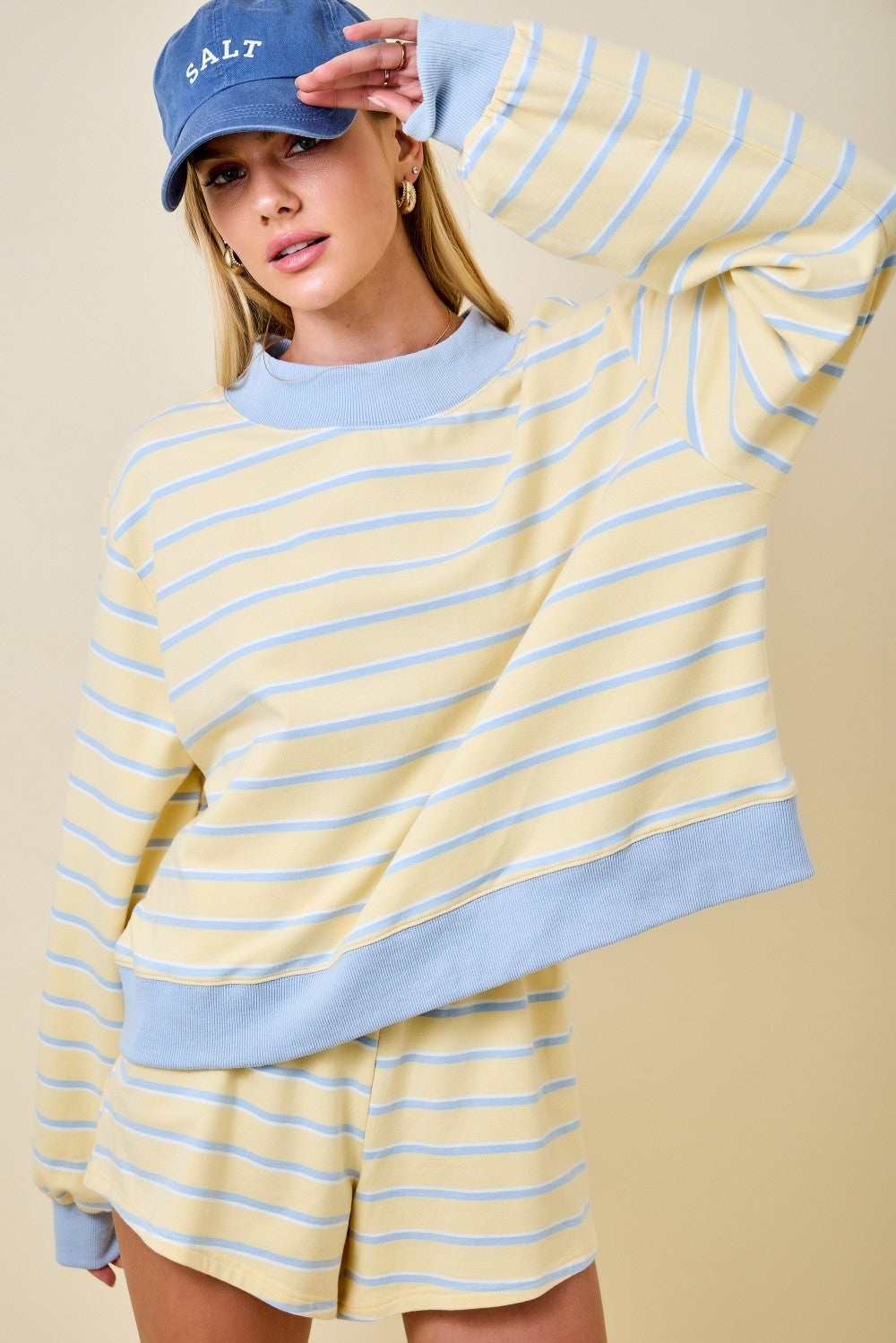 Woman wearing a yellow and light blue striped mockneck sweatshirt with matching lounge shorts.