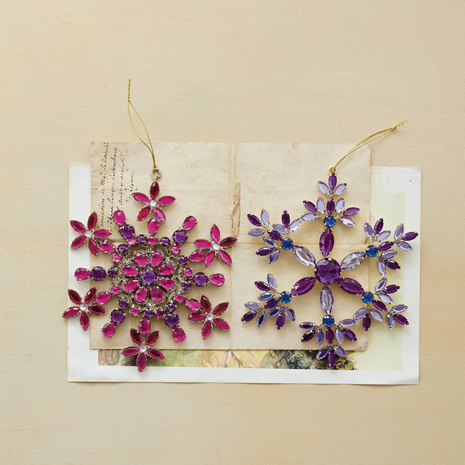 Two metal snowflake ornaments with pink and purple acrylic jewels on a vintage paper background.