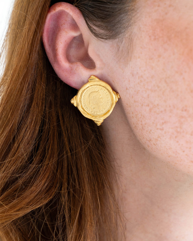 Close-up of a person wearing a gold intaglio coin earring with a 1948 profile design.