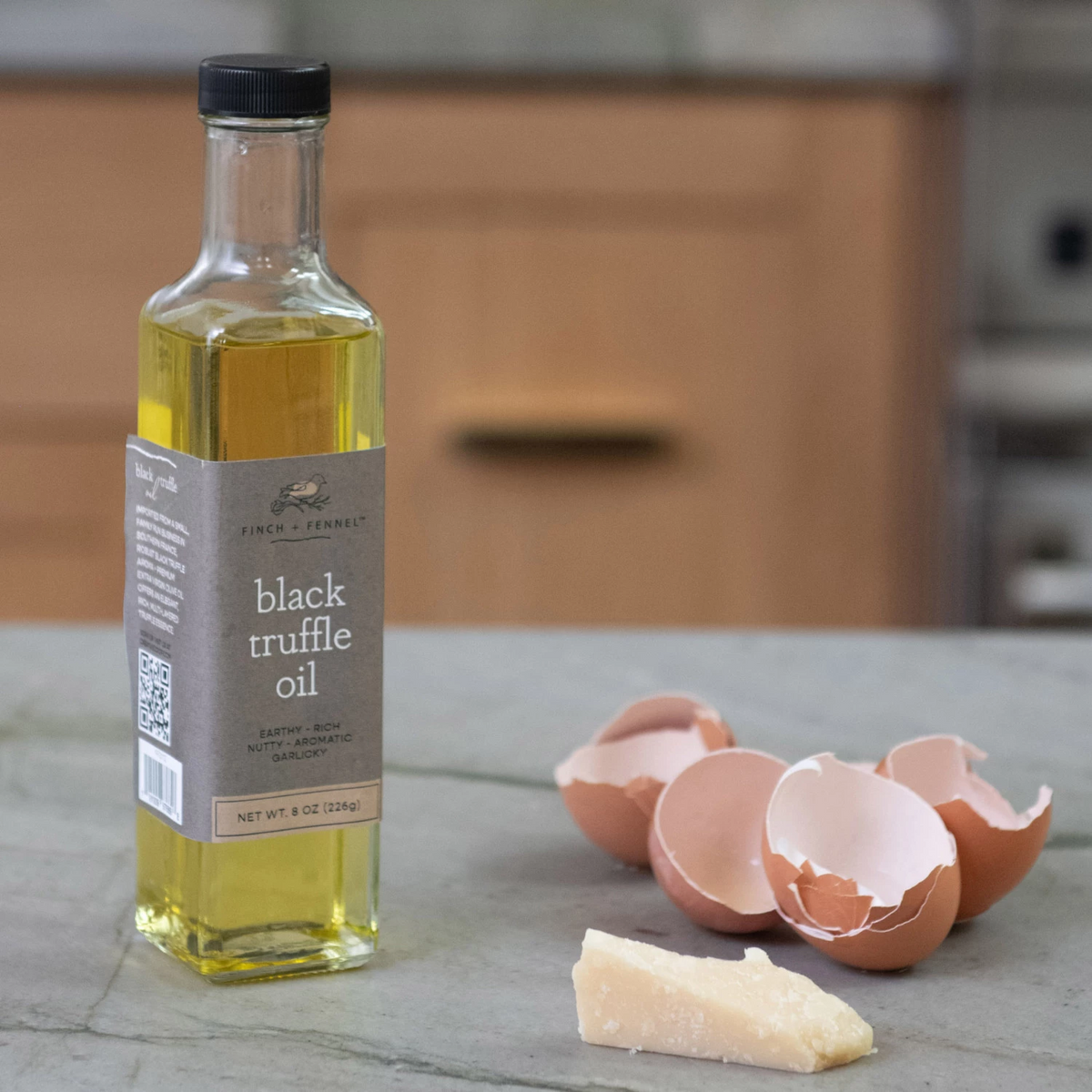 A bottle of Finch + Fennel Black Truffle Oil next to eggshells and a wedge of parmesan cheese.