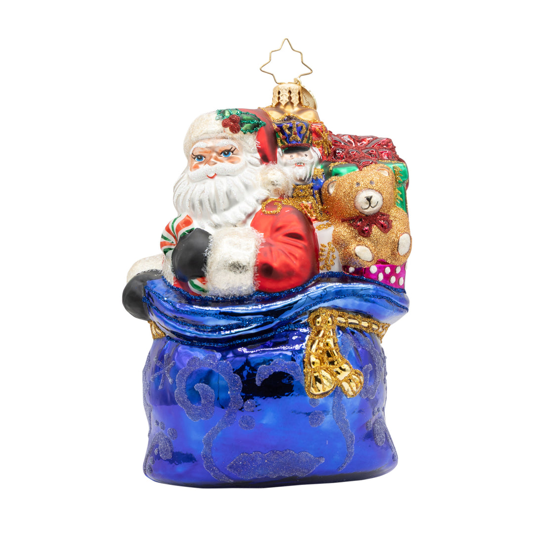 Kris Kringle’s Bundle glass ornament featuring Santa with a blue toy sack, teddy bear, and gifts.