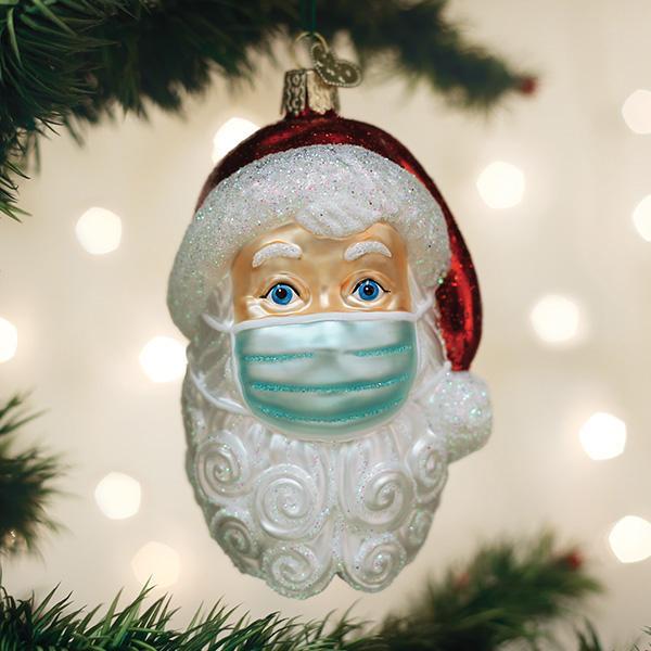 Glass Santa Claus ornament wearing a blue face mask and red glitter hat on a Christmas tree.