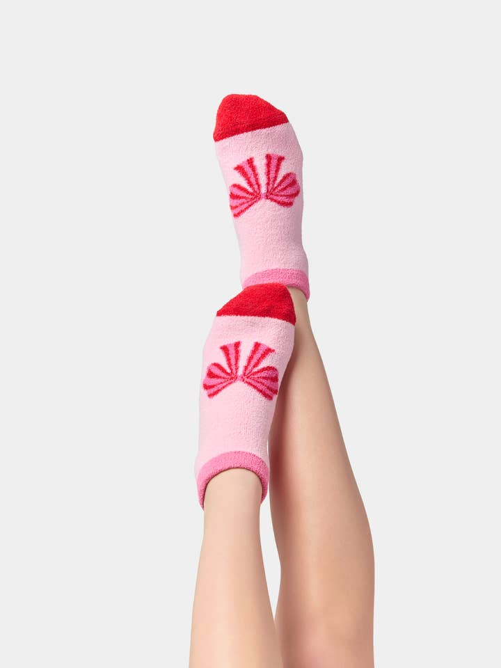 A pair of pink fuzzy ankle socks with red toe caps and a red bow design on the top.