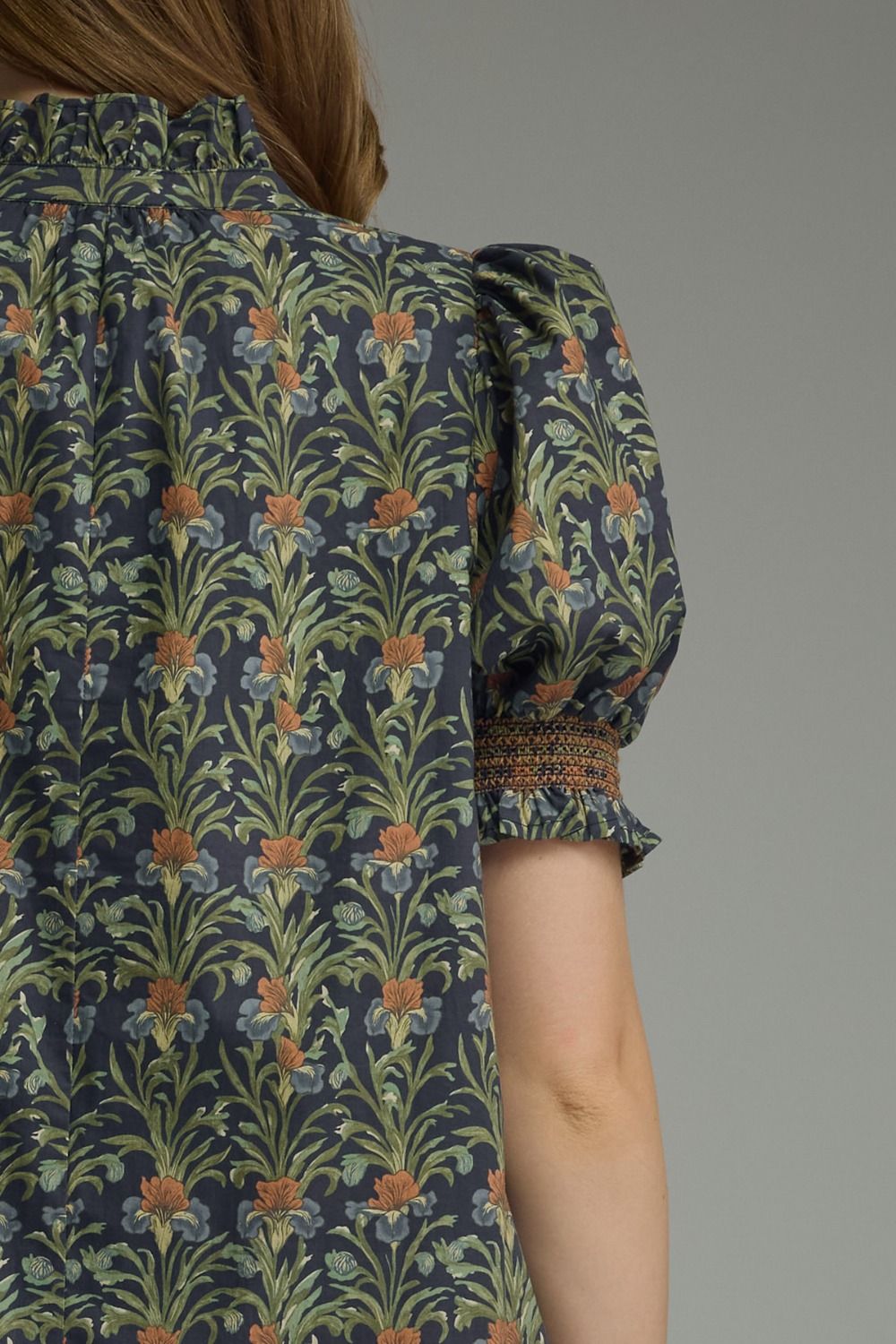 Back view of a navy midi dress with a green and orange floral print and smocked puff sleeves.
