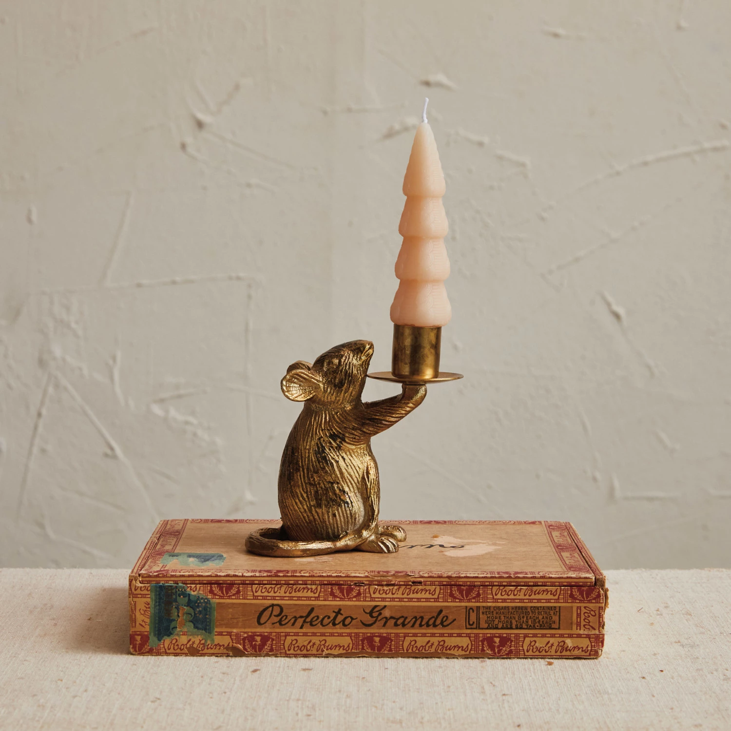 Antique gold cast aluminum mouse taper candle holder sitting on a vintage cigar box.