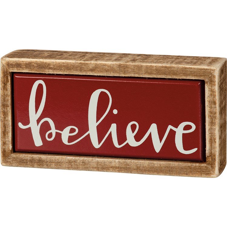 Small wooden box sign with a red background and the word 'believe' in white script lettering.