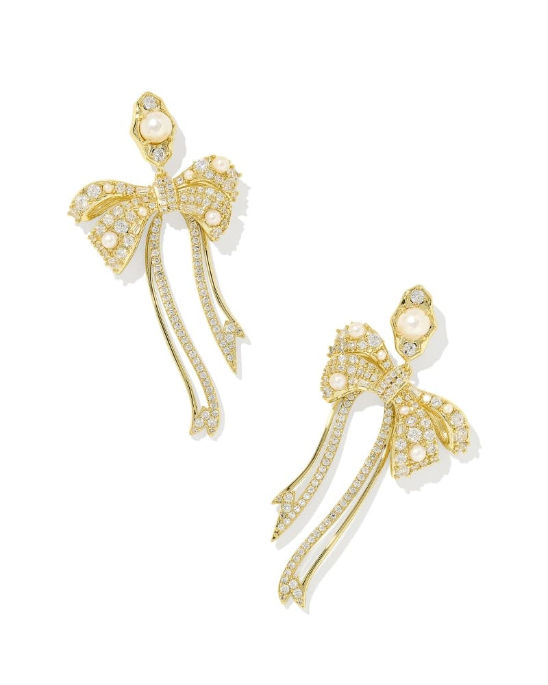 Oversized asymmetrical gold bow statement earrings featuring white pearls and crystals on ear posts.