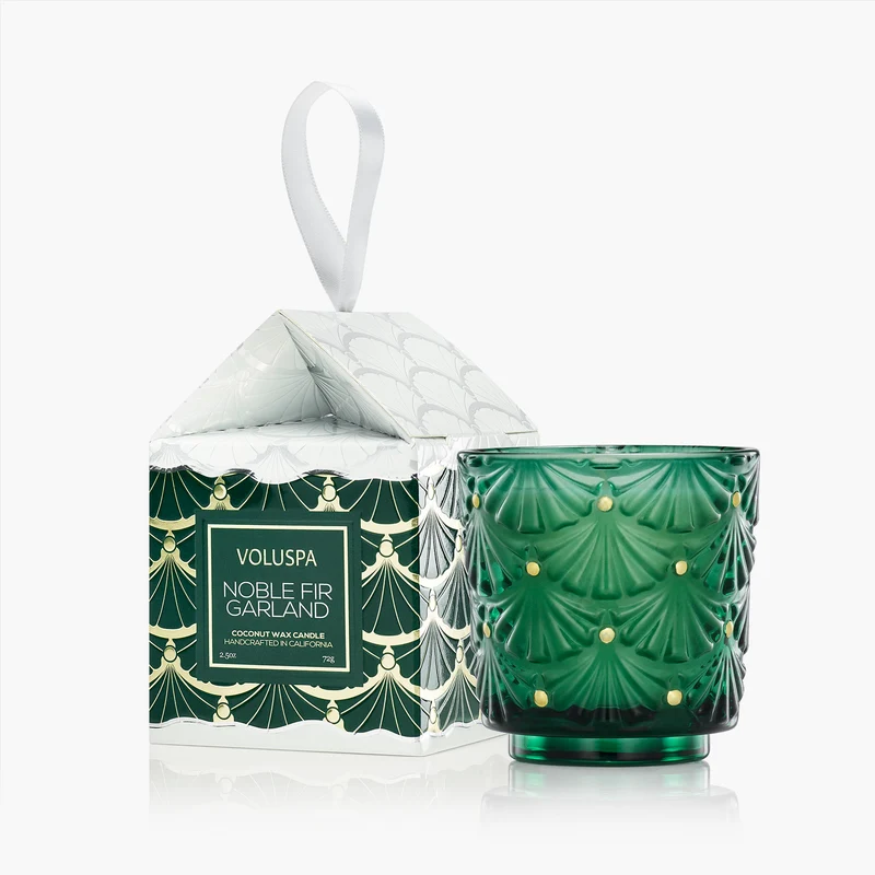 Voluspa Noble Fir Garland 2.5oz candle in a green glass pedestal jar next to its ornament gift box.