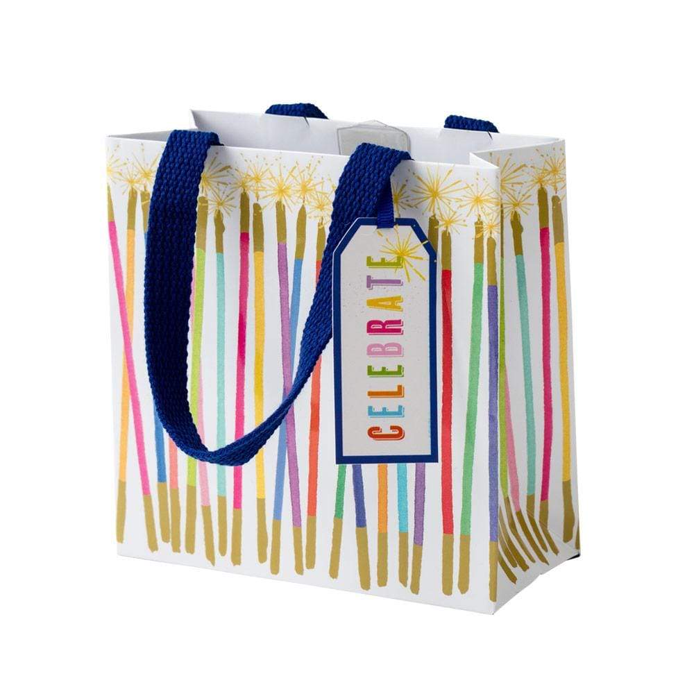 Small square gift bag with a white background, decorated with colorful vertical stripes resembling candles and gold accents. A blue tag reads 'CELEBRATE'.