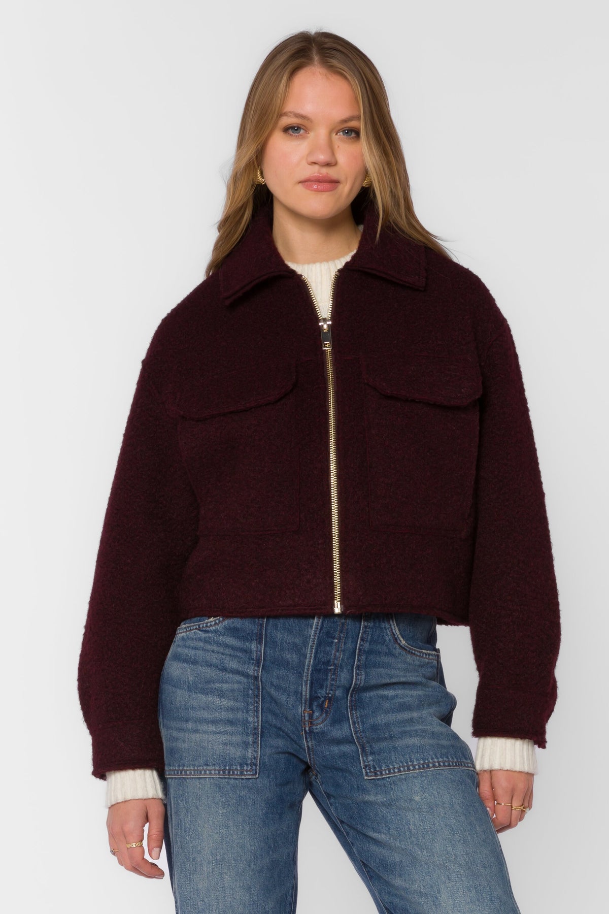 Woman wearing the Galinda Jacket, a burgundy bouclé zip-front cropped jacket with flap pockets.
