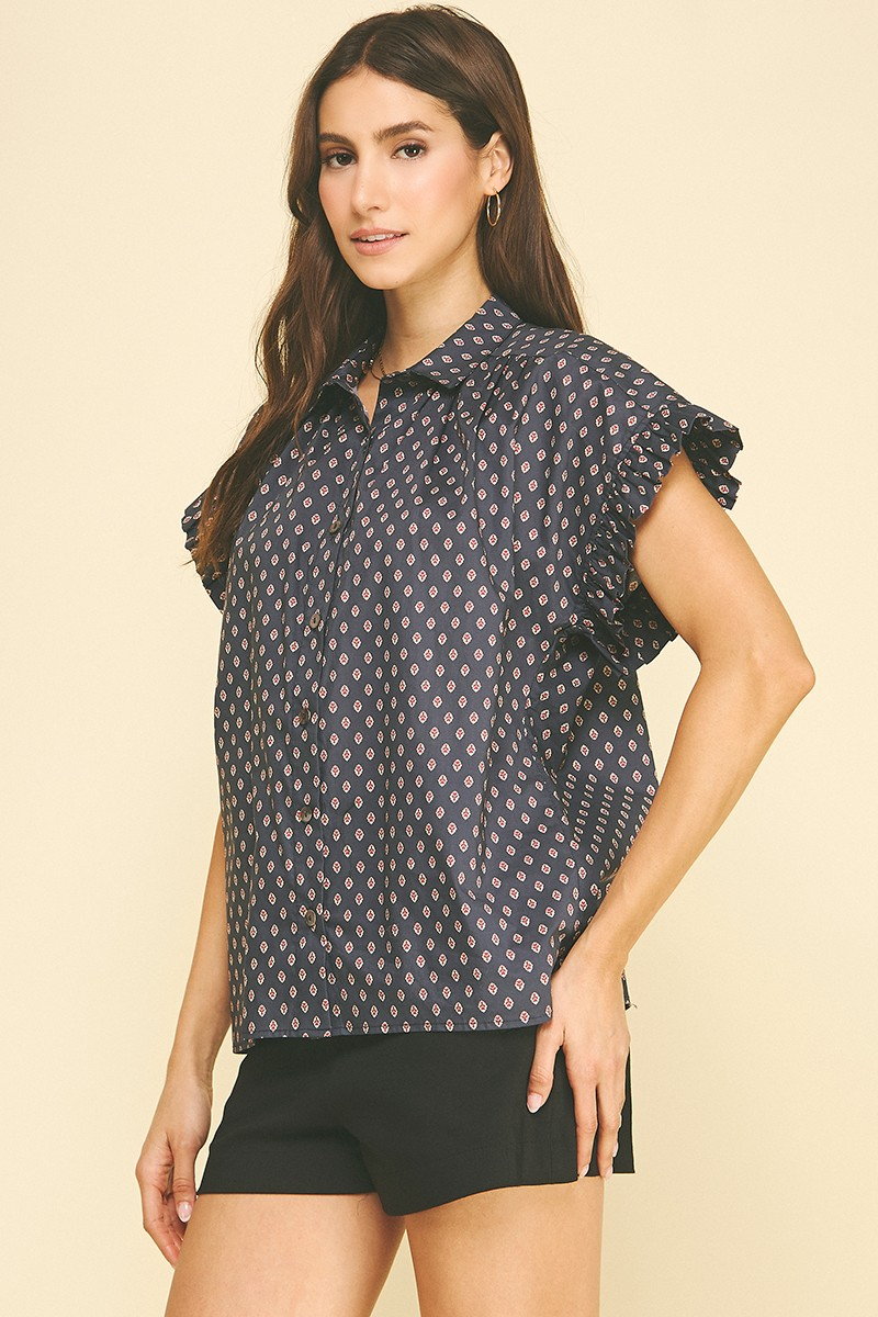 Woman wearing a navy blue geometric diamond print button-down shirt with ruffled cap sleeves.
