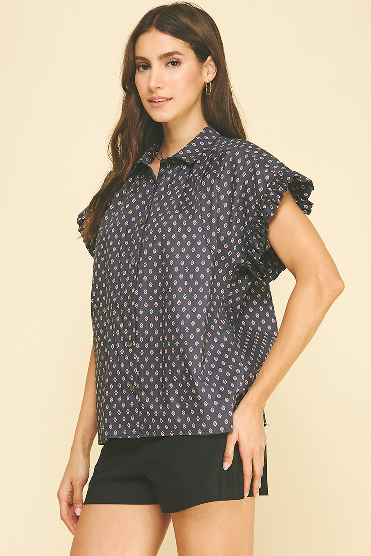 Woman wearing a navy blue geometric diamond print button-down shirt with ruffled cap sleeves.